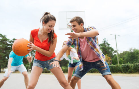 Happy teenagers playing basketball outdoors