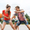 Happy teenagers playing basketball outdoors